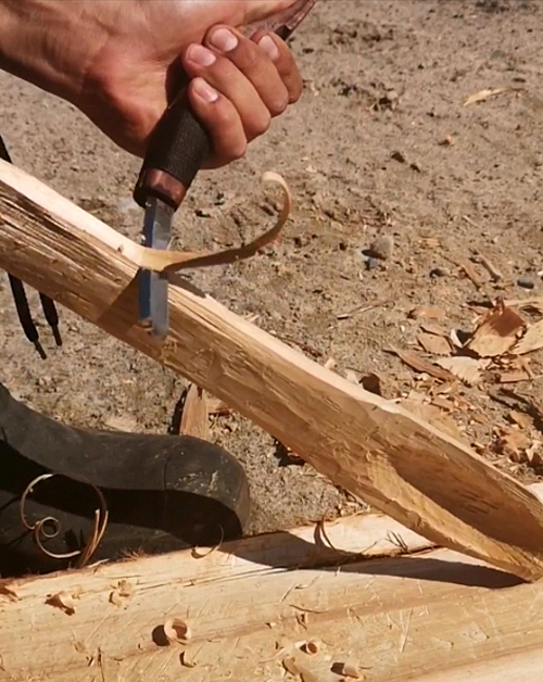 hand holding knife and scraping wood stick