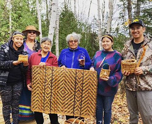 Group of Indigenous young people and elders holding hand woven baskets and mats outside